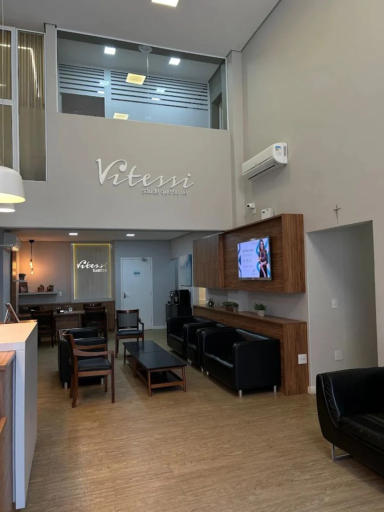Sala principal da Clínica Vitessi, com pé-direito alto, poltronas e logo da clínica na parede
